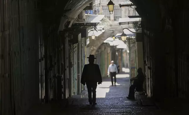 People walk in an nearly empty alley in Jerusalem's Old City as Israel's Home Front Command banned public gatherings following an Israeli military strike on Iran, in Jerusalem's Old City, Friday, June 13, 2025. (AP Photo/Mahmoud Illean)