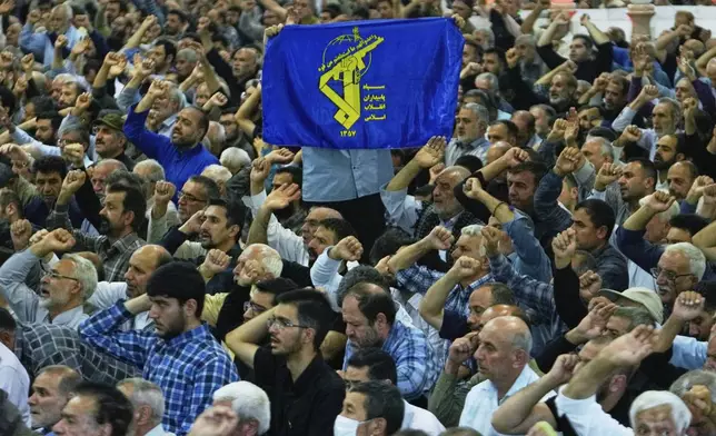 An Iranian worshipper holds up a banner containing the Revolutionary Guard emblem as the others chant slogans during Friday prayers ceremony at Tehran University campus in Tehran, Iran, Friday, June 13, 2025. (AP Photo/Vahid Salemi)