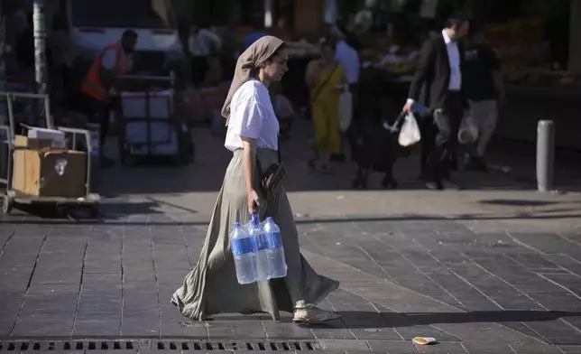 A woman carries water at the Mahane Yehuda market in Jerusalem ahead of Shabbat, Friday, June 13, 2025. (AP Photo/Ohad Zwigenberg)