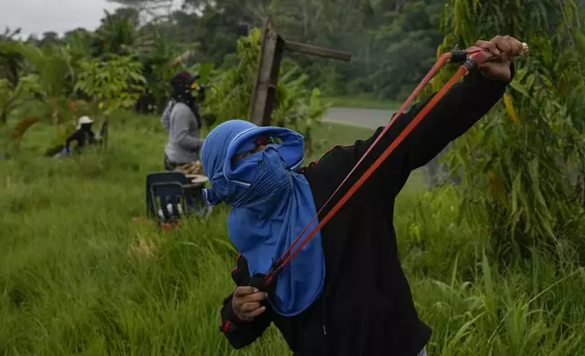 An anti-government protester aims a slingshot during clashes with police while blocking a highway in the Indigenous Embera community of Arimae, Panama, during a demonstration against a pension reform law and a security agreement with the United States involving the Panama Canal, Thursday, June 5, 2025. (AP Photo/Matias Delacroix)