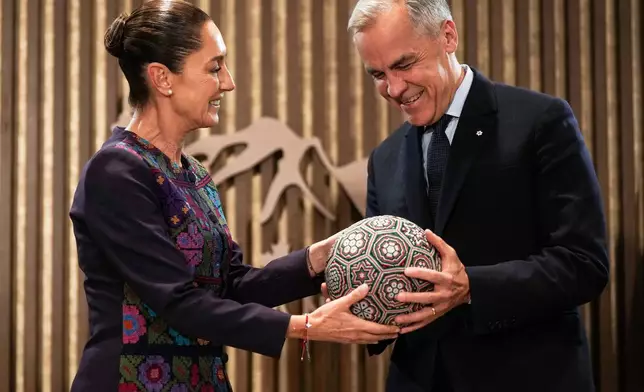 Mexican President Claudia Sheinbaum, left, presents Canada's Prime Minister Mark Carney a soccer ball with beaded Huichol art on it before a meeting at the G7 Summit in Kananaskis, Alberta, Tuesday, June 17, 2025. (Darryl Dyck/The Canadian Press via AP)