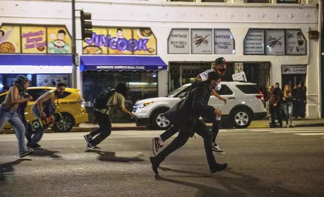 Protesters run to avoid being kettled by police during protests over the Trump administration's immigration raids in Los Angeles, Monday, June 9, 2025. (AP Photo/Ethan Swope)