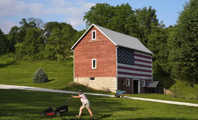 Stacey Schmitt mows in front of a flag-painted barn Saturday, June 7, 2025, on her family farm near Linwood, Kan. (AP Photo/Charlie Riedel)