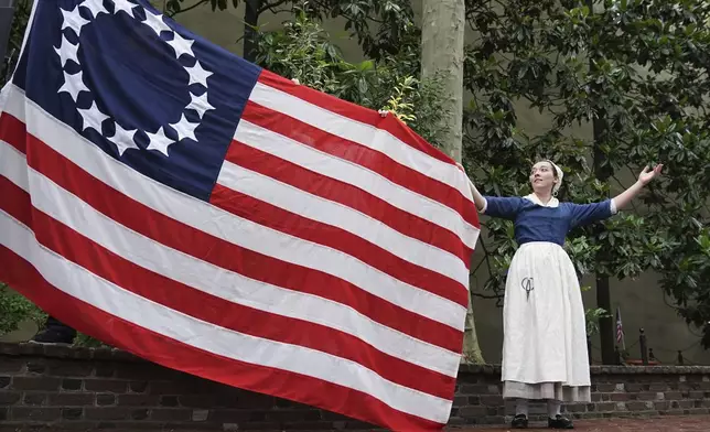 Madeline Burk, portraying Betsy Ross, holds a flag as it is hoisted up at the Betsy Ross House in Philadelphia, Monday, June 9, 2025. (AP Photo/Matt Rourke)
