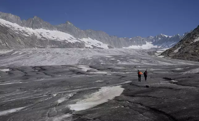 Matthias Huss, of the Federal Institute of Technology in Zurich and glacier monitoring group GLAMOS, and Monica Ursina Jaeger arrive at the Rhone glacier near Goms, Switzerland, June 10, 2025. (AP Photo/Matthias Schrader)