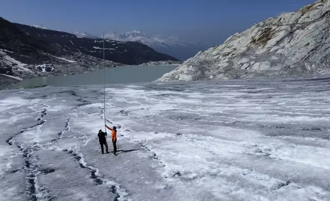 Matthias Huss, of the Federal Institute of Technology in Zurich and glacier monitoring group GLAMOS, and Monica Ursina Jaeger make measurements at the Rhone glacier near Goms, Switzerland, June 10, 2025. (AP Photo/Matthias Schrader)