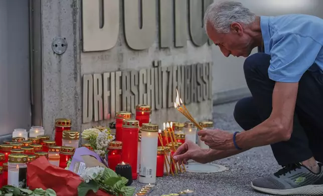 A man lights candles at the entrance of a school, after a deadly shooting there, in Graz, Austria, Tuesday, June 10, 2025. (AP Photo/Heinz-Peter Bader)
