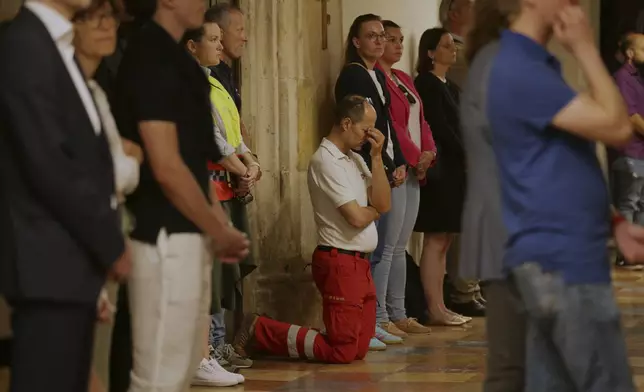 A member of rescue services knees on the floor and pray during a memorial service, following a shooting at a school, at the cathedral in Graz, Austria, Tuesday, June 10, 2025. (AP Photo/Heinz-Peter Bader)