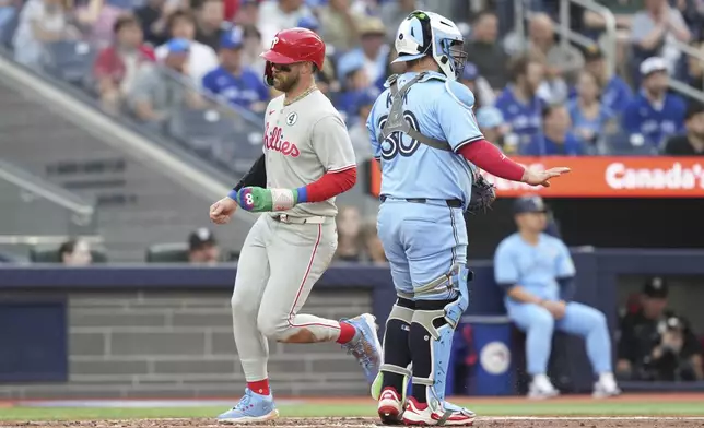 Philadelphia Phillies' Bryce Harper (3) crosses home plate in front of Toronto Blue Jays catcher Alejandro Kirk (30) after scoring off a throwing error from Blue Jays' Addison Barger during the second inning of a baseball game in Toronto, Tuesday June 3, 2025. (Chris Young/The Canadian Press via AP)