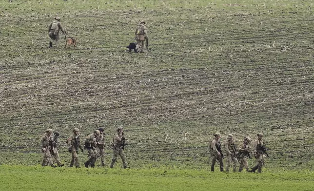 Members of law enforcement agencies walk through a field near a vehicle suspected to belong to shooting suspect, Vance Boelter, Sunday, June 15, 2025, in Belle Plaine, Minn. (AP Photo/George Walker IV)