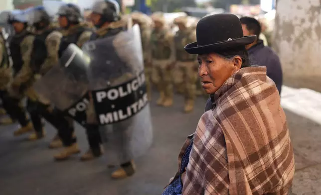 A woman observes military police patrolling after police spent days clearing roadblocks set up by supporters of Bolivia's former President Evo Morales who want him to be able to run for president again in Llallagua, Bolivia, Friday, June 13, 2025. (AP Photo/Juan Karita)