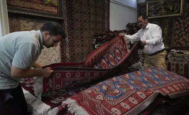 Carpet sellers adjust carpets in their shop in northern Tehran, Iran, Monday, June 2, 2025. (AP Photo/Vahid Salemi)