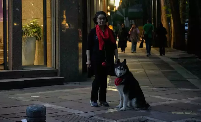 A woman stands with her dog, Lucifer, on a sidewalk in northern Tehran, Iran, Monday, June 2, 2025. (AP Photo/Vahid Salemi)