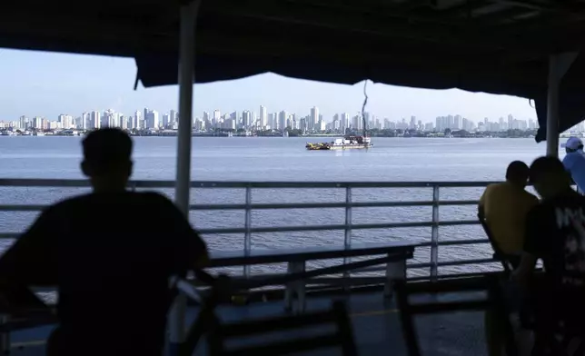 FILE - People look out at the coast of Belem, Brazil, as a boat nears shore, March 23, 2025. (AP Photo/Jorge Saenz, File)