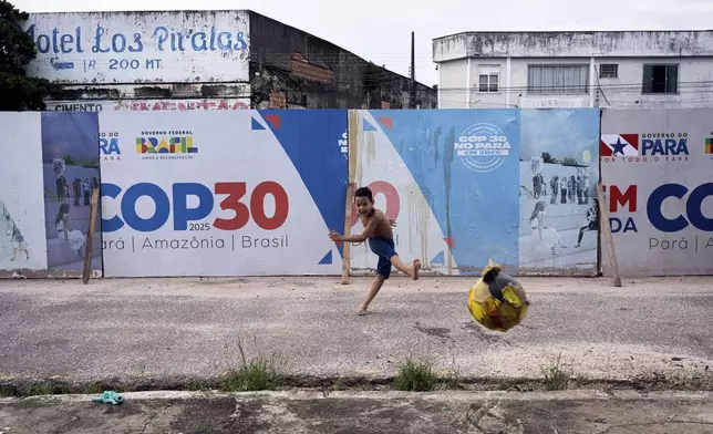 FILE - A boy kicks a soccer ball near signage for the COP30 U.N. Climate Conference in Belem, Brazil, March 23, 2025. (AP Photo/Jorge Saenz, File)