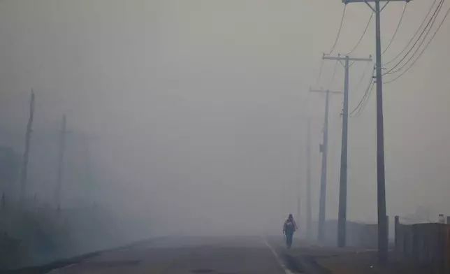 FILE - A person walks on the BR-319 highway through smoke from a forest fire that reaches Careiro Castanho in Brazil's Amazonas state, Sept. 6, 2023. (AP Photo/Edmar Barros, File)