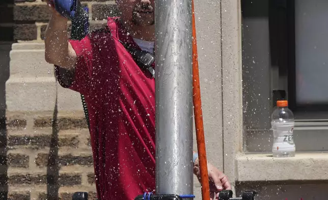 A Chicago Cubs security guard cools off under a sprinkler provided by a Chicago Fire Department outside of Wrigley Field before a baseball game between the Seattle Mariners and the Chicago Cubs in Chicago, Sunday, June 22, 2025. (AP Photo/Nam Y. Huh)