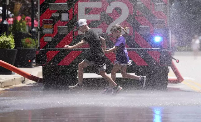 Children run through water sprayed by a fire truck to cool off outside Busch Stadium before the start of a baseball game between the St. Louis Cardinals and the Cincinnati Reds Sunday, June 22, 2025, in St. Louis. (AP Photo/Jeff Roberson)