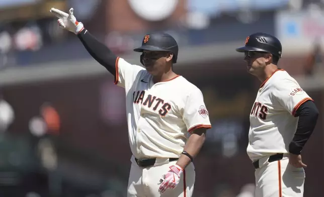 San Francisco Giants' Rafael Devers, left, gestures next to first base coach Mark Hallberg after hitting a single during the eighth inning of a baseball game against the Cleveland Guardians in San Francisco, Thursday, June 19, 2025. (AP Photo/Jeff Chiu)