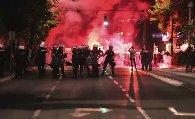 Riot police block a street as anti-government protesters light flares at the end of a rally pressing for an early election after nearly eight months of almost daily anti-corruption demonstrations that have shaken the populist government of President Aleksandar Vucic, in Belgrade, Serbia, Saturday, June 28, 2025. (AP Photo/Darko Vojinovic)