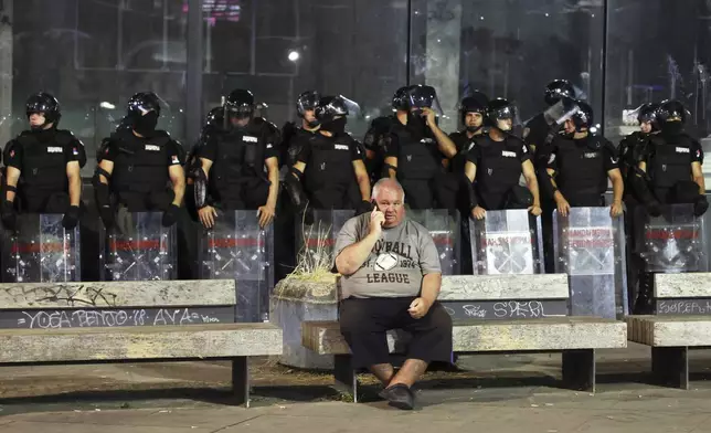 A man speaks on a mobile phone as riot police guards the area at the end of an anti-government rally pressing for an early election after nearly eight months of almost daily anti-corruption demonstrations that have shaken the populist government of President Aleksandar Vucic, in Belgrade, Serbia, Saturday, June 28, 2025. (AP Photo/Marko Drobnjakovic)