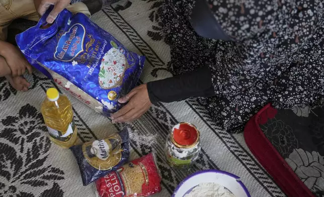 Anwaar Saleh, 32, displays the donated food her husband, Omar al-Hobi, collected at a distribution center run by private contractor the Gaza Humanitarian Foundation in the southern Gaza Strip, after he arrived at their family's tent in Khan Younis, Tuesday, June 10, 2025. (AP Photo/Abdel Kareem Hana)