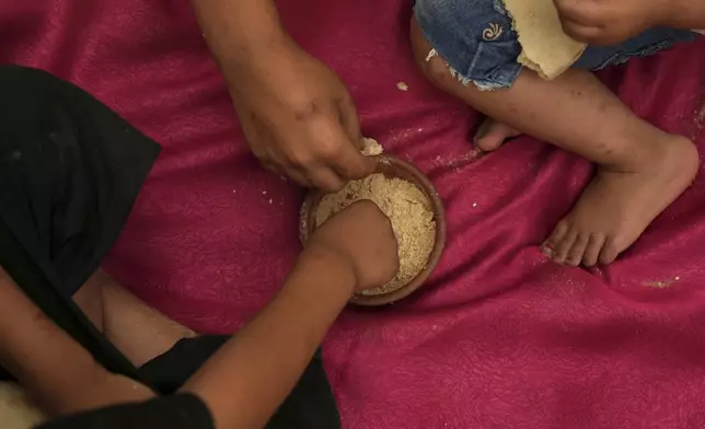 The children of Jamil Atili, 51, eat ground lentils after their father returned empty-handed from an attempt to collect donated food at a distribution center run by private contractor the Gaza Humanitarian Foundation in the southern Gaza Strip, in Khan Younis, Wednesday, June 11, 2025. (AP Photo/Abdel Kareem Hana)