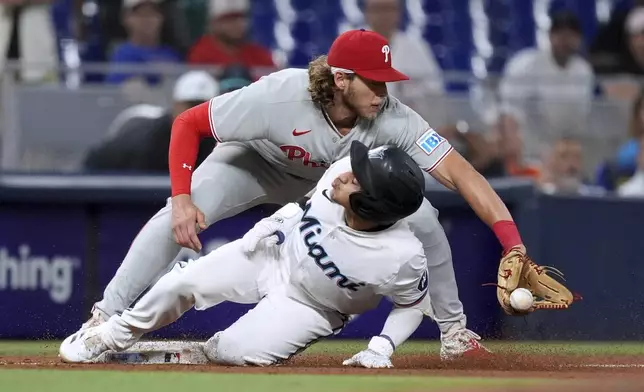 Miami Marlins' Javier Sanoja slides into second base past Philadelphia Phillies third baseman Alec Bohm after hitting a triple in the sixth inning of a baseball game, Tuesday, June 17, 2025, in Miami. (AP Photo/Rebecca Blackwell)