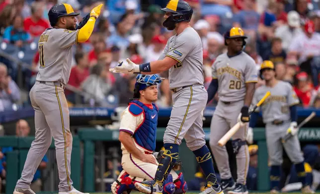 Milwaukee Brewers' Rhys Hoskins, right, celebrates his second three-run home run with Jackson Chourio, left, as Philadelphia Phillies catcher J.T. Realmuto, center, looks on during the fourth inning of a baseball game against the Philadelphia Phillies, Saturday, May 31, 2025, in Philadelphia. (AP Photo/Chris Szagola)
