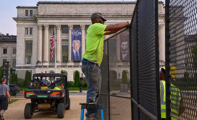 Workers install security fencing on the National Mall, Tuesday, June 10, 2025, outside the USDA Whitten Building where a large photograph of President Donald Trump is draped, in Washington. (AP Photo/Jacquelyn Martin)