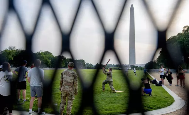 Seen through security fencing, Army Sgt. Chase Beasley, left, watches as Army Spc. Steven Holmes, right, take a swing as they sit-in on a game of softball with congressional staffers on the National Mall, during preparations for an upcoming military parade commemorating the Army's 250th anniversary and coinciding with President Donald Trump's 79th birthday, Thursday, June 12, 2025, in Washington. (AP Photo/Rod Lamkey, Jr.)