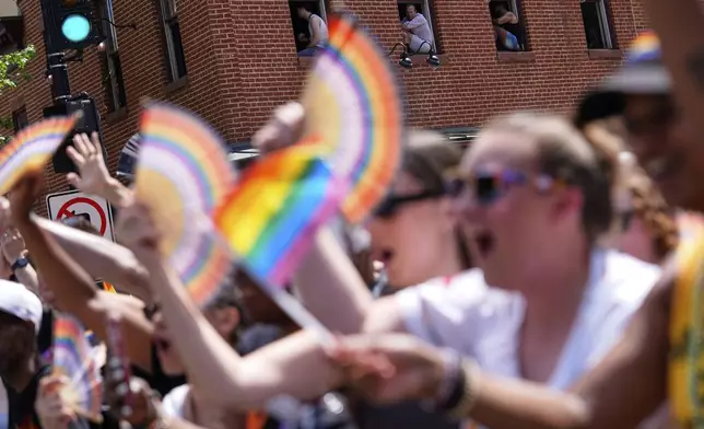 People sit in the windows sills of a building as the World Pride parade passes, Saturday, June 7, 2025, in Washington. (AP Photo/Julia Demaree Nikhinson)
