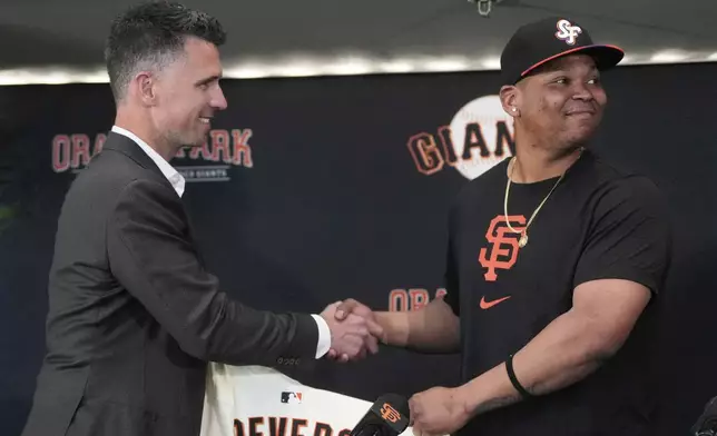 San Francisco Giants President of Baseball Operations Buster Posey, left, shakes hands with Rafael Devers during a news conference before a baseball game between the Giants and the Cleveland Guardians in San Francisco, Tuesday, June 17, 2025. (AP Photo/Jeff Chiu)