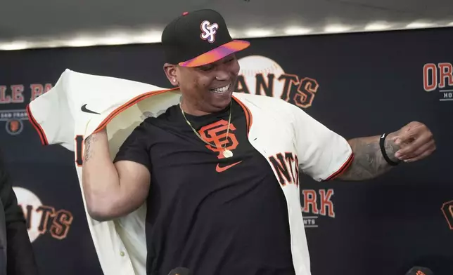 San Francisco Giants' Rafael Devers puts on a jersey at a news conference before a baseball game against the Cleveland Guardians in San Francisco, Tuesday, June 17, 2025. (AP Photo/Jeff Chiu)