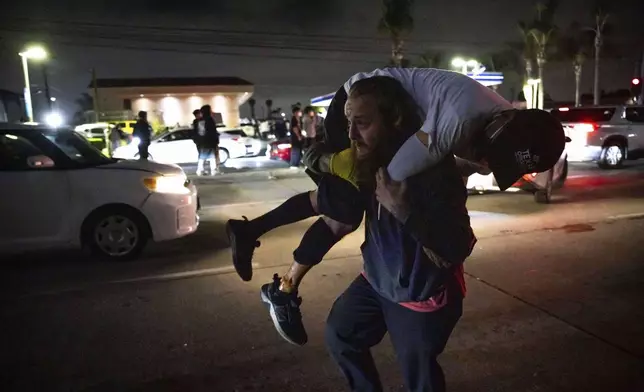 A person carries an injured protester to cover during a protest in Compton, Calif., Saturday, June 7, 2025, after federal immigration authorities conducted operations. (AP Photo/Ethan Swope)