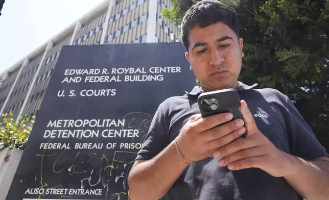 Alejandro Barranco checks his phone as he arrives to check on his father Narciso, who was detained by federal agents, outside the Metropolitan Detention Center on Monday, June 23, 2025, in Los Angeles. (AP Photo/Damian Dovarganes)