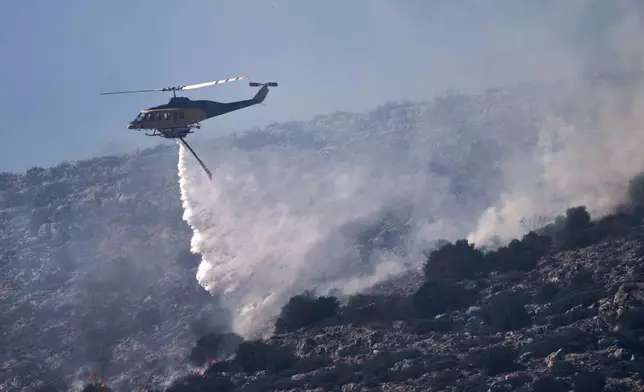 A firefighting helicopter drops water while battling a blaze in the seaside area of Charakas, south of Athens, Thursday, June 26, 2025, as authorities evacuate five locations during Greece's first summer heatwave with temperatures nearing 40 degrees Celsius (104 Fahrenheit). (AP Photo/Thanassis Stavrakis)