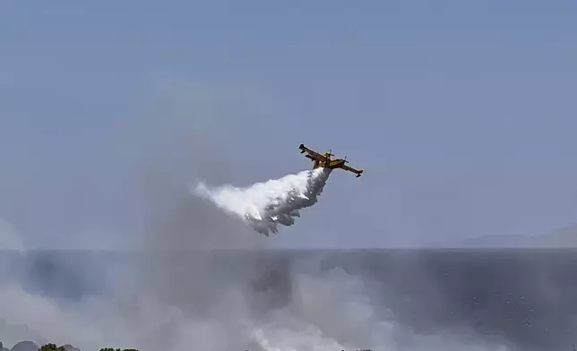A Firefighting plane drops water while battling a blaze in the seaside area of Palaia Fokaia, south of Athens, Thursday, June 26, 2025, as authorities evacuate five locations during Greece's first summer heatwave with temperatures nearing 40 degrees Celsius (104 Fahrenheit).(AP Photo/Giorgos Delveroudis)