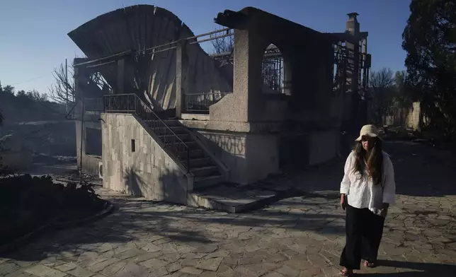 Lillian Tsertou walks in front of her burned down house in Thymari, south of Athens, Thursday, June 26, 2025, as authorities evacuate five locations during Greece's first summer heatwave with temperatures nearing 40 degrees Celsius (104 Fahrenheit). (AP Photo/Thanassis Stavrakis)