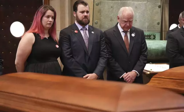 CORRECTS NAME TO SOPHIE HORTMAN FROM ALINA BACHMAN - Sophie Hortman, Colin Hortman, and Gov. Tim Walz stand behind the caskets of Melissa and Mark Hortman during funeral services for Mark and Melissa Hortman at the Basilica of St. Mary in Minneapolis, Minn., on Saturday, June 28, 2025. (Alex Kormann/Star Tribune via AP, Pool)