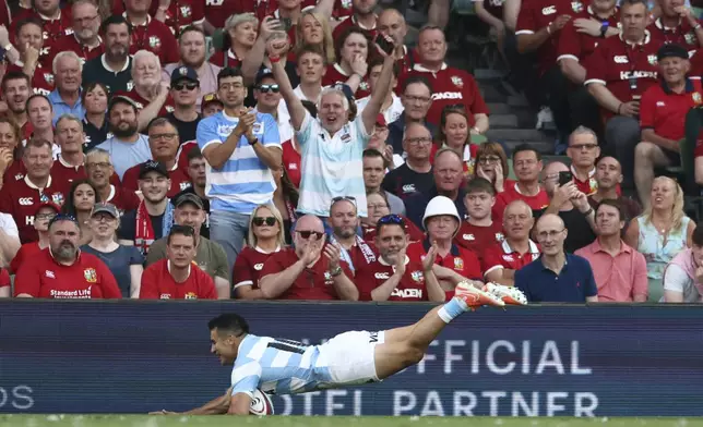 Argentina's Tomas Albornoz dives over the line to score a try, as two Argentine fans celebrate in the stands behind, during the Rugby Union international match between the British and Irish Lions and Argentina, at the Aviva Stadium in Dublin, Friday, June 20, 2025. (AP Photo/Peter Morrison)