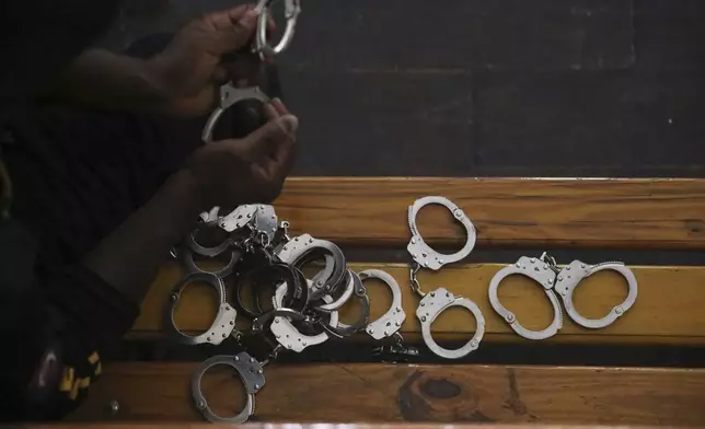 A police officer holds up the handcuffs removed from Colombians and Haitians accused of involvement in the 2021 assassination of Haitian President Jovenel Moise, in court in Port-au-Prince, Haiti, Monday, June 2, 2025. (AP Photo/Odelyn Joseph)