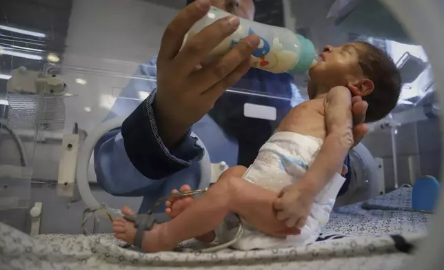 A nurse feeds a prematurely born baby lying in an incubator at the neonatal intensive care unit of Nasser Hospital in Khan Younis, southern Gaza Strip, Thursday, June 19, 2025. (AP Photo/Mariam Dagga)