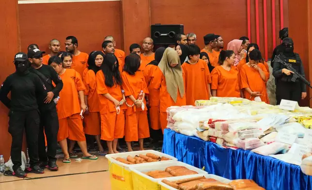 Indonesian police officers stand guard near suspects and various drugs seized in a nationwide crackdown in the past few months, before the start of a press conference at the Indonesian Customs headquarters in Jakarta, Indonesia, Monday, June 23, 2025. (AP Photo/Achmad Ibrahim)
