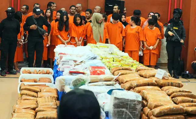 Indonesian police officers stand guard near suspects and various drugs seized in a nationwide crackdown in the past few months, before the start of a press conference at the Indonesian Customs headquarters in Jakarta, Indonesia, Monday, June 23, 2025. (AP Photo/Achmad Ibrahim)