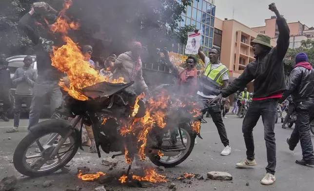 Protesters gesture in-front of a burning motorcycle during a demonstration over the death of blogger Albert Ojwang in police custody, in downtown Nairobi, Kenya, Tuesday, June 17, 2025. (AP Photo/Brian Inganga)