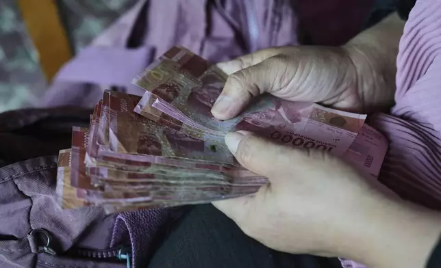 Nina Herlina counts rupiah banknotes she earns from selling livestock ahead of the Eid al-Adha festival, at her stall in Jakarta, Indonesia, Wednesday, June 4, 2025.(AP Photo/Achmad Ibrahim)