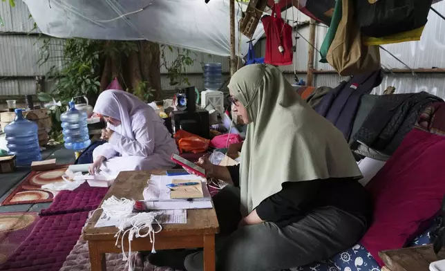 Nina Herlina, right, checks her mobile phone as she waits for customer with her daughter Camelia, at her livestock stall in Jakarta, Indonesia, Monday, June 2, 2025. (AP Photo/Achmad Ibrahim)