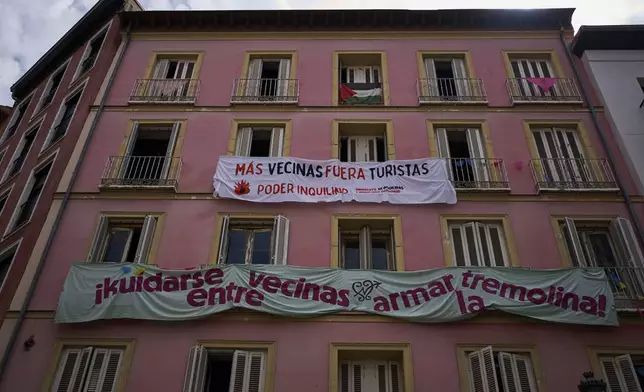 FILE - Banners against tourist holiday rentals hang on the facade of a building in downtown Madrid, Spain, June 3, 2025. The writing in Spanish reads: "More neighbors, fewer tourists. Tenant power," and "Looking out for each other as neighbors, stirring things up." (AP Photo/Manu Fernandez, File)