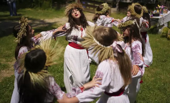 Girls wearing crowns made of flowers dance during an event inspired by pre-Christian traditions, in which fairies, called in Romanian "Sanziene," come to earth around the summer solstice bringing fertility to land and beings, at the Dimitrie Gusti Village Museum in Bucharest, Romania, Tuesday, June 24, 2025. (AP Photo/Andreea Alexandru)